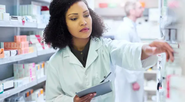 a pharmacy technician searching through various prescription medications after completing a pharmacy technician training program offered by her employer